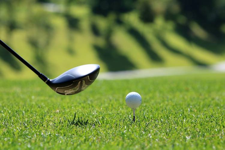 a golf driver held by an out of frame golfer next to a ball on a tee